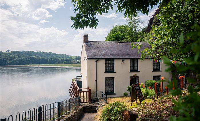 View of the front of the Boathouse from a pathway at the side of a small garden. The Taf estuary and Sir John's Hill can be seen in the distance behin